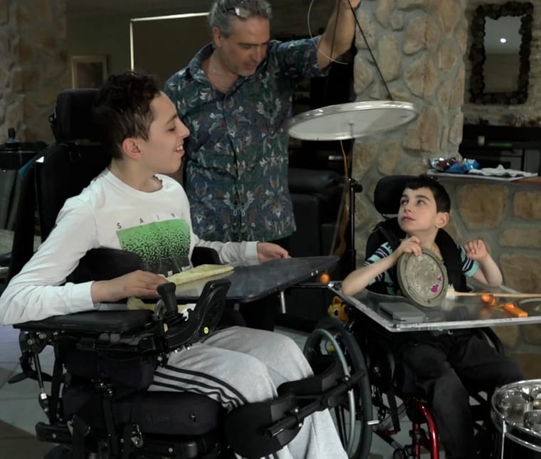 A Safe in Sound musician plays a cymbal with two young brothers in their wheelchairs