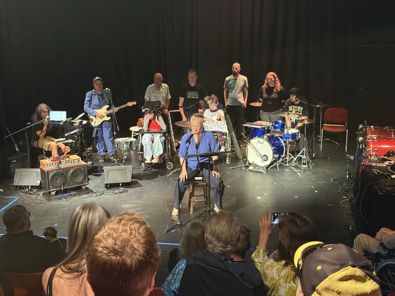 A mixed-ability ensemble of guitarists, drummers and vocalists performing on stage to an audience